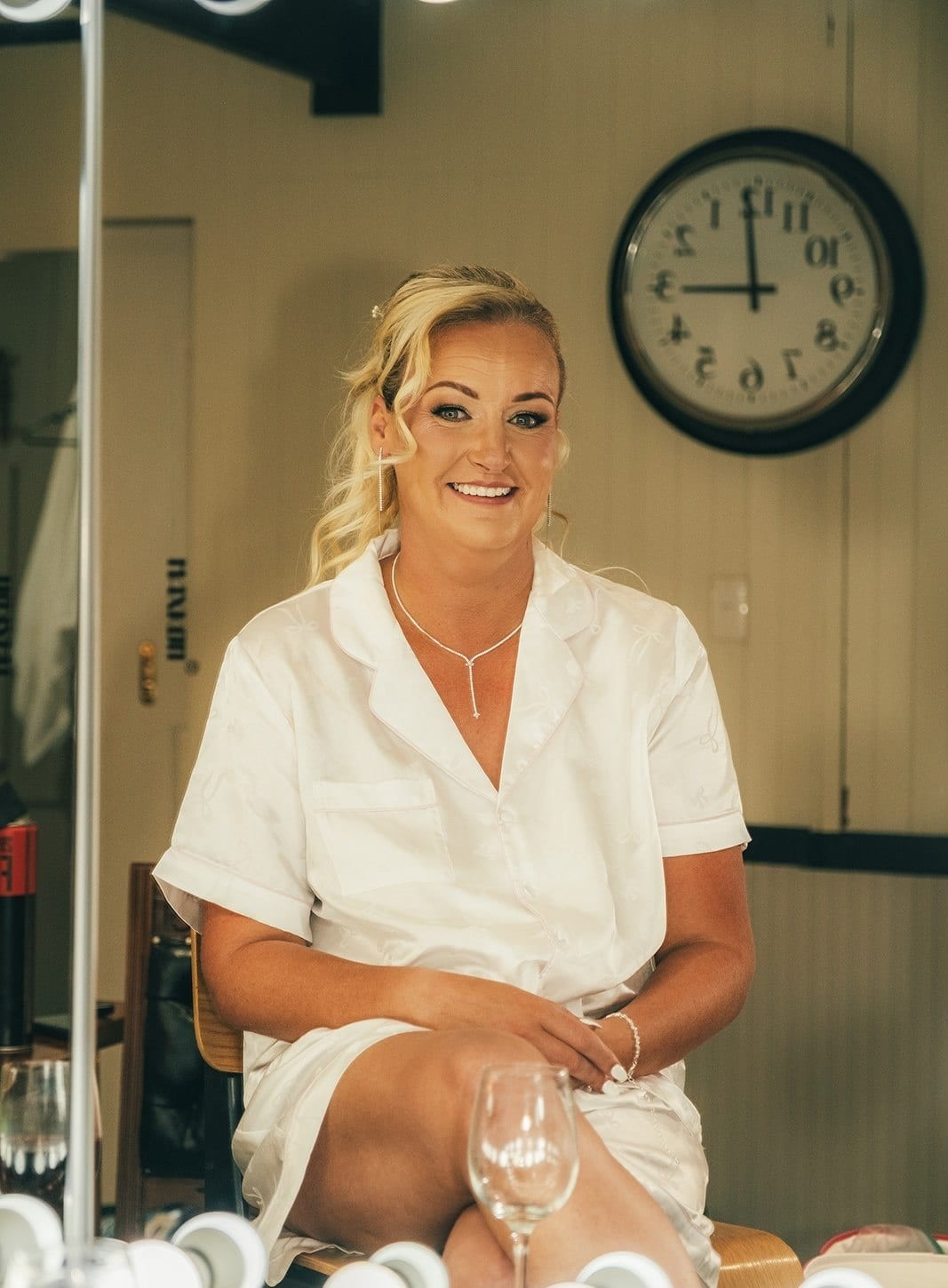 Jenna smiling in a white robe at the dressing table, a wall clock behind her