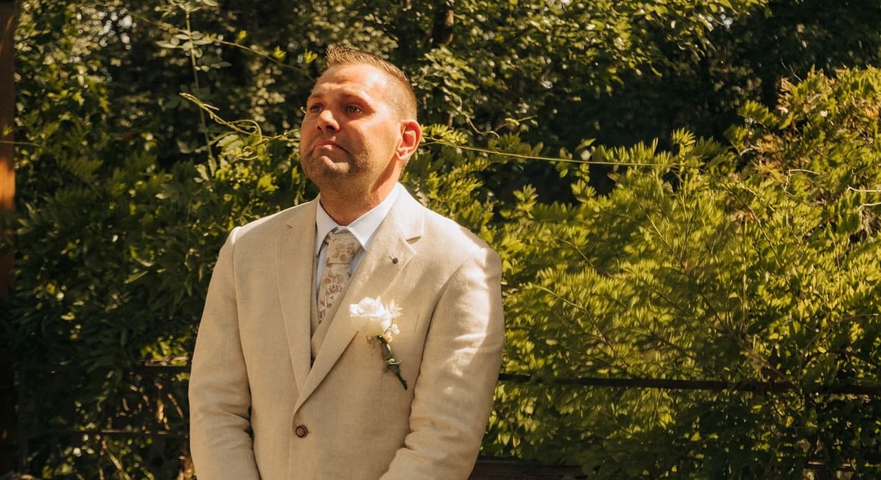 Nick in his cream suit looking up as he waits for Jenna under the pergola