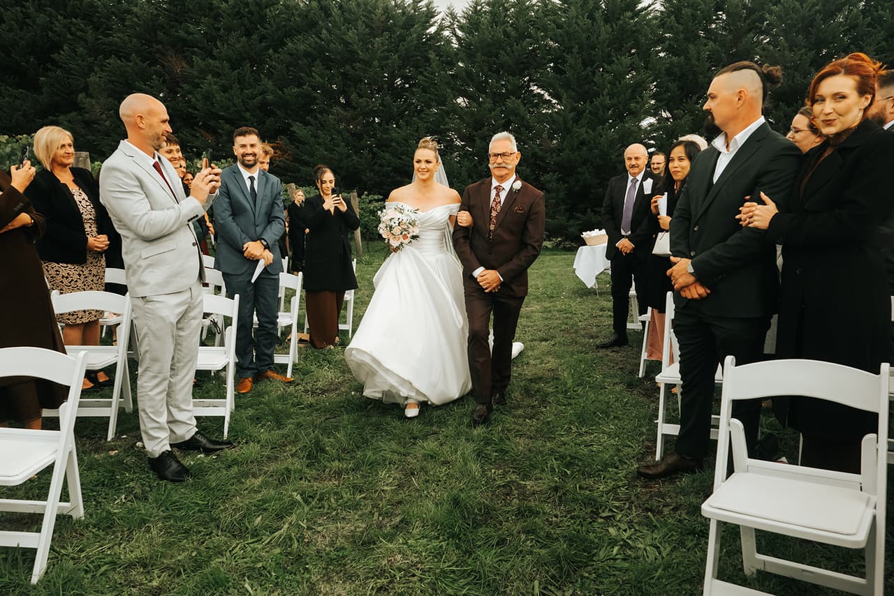 Jessica walking down the aisle on her dad’s arm as the guests stand and smile