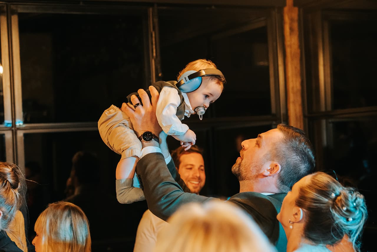 Max lifting a baby in blue ear muffs high above his head on the dance floor