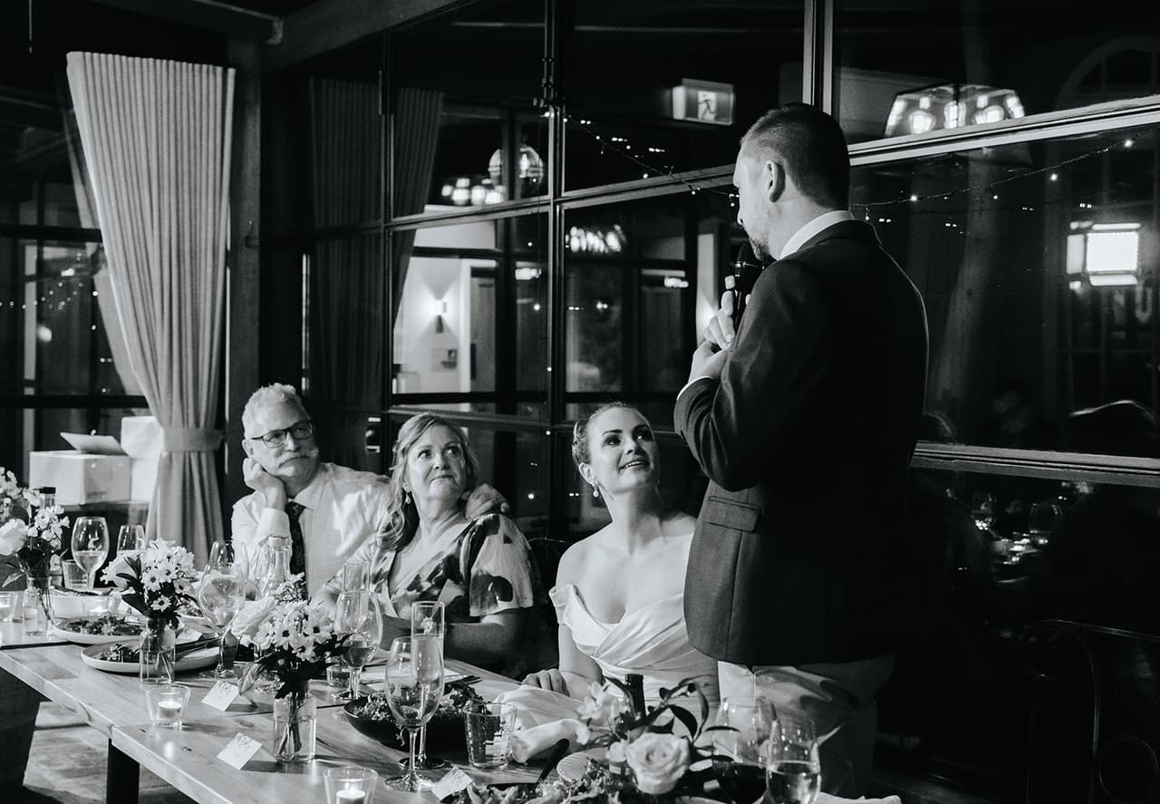 Black and white photo of Max giving his speech as Jessica looks up at him