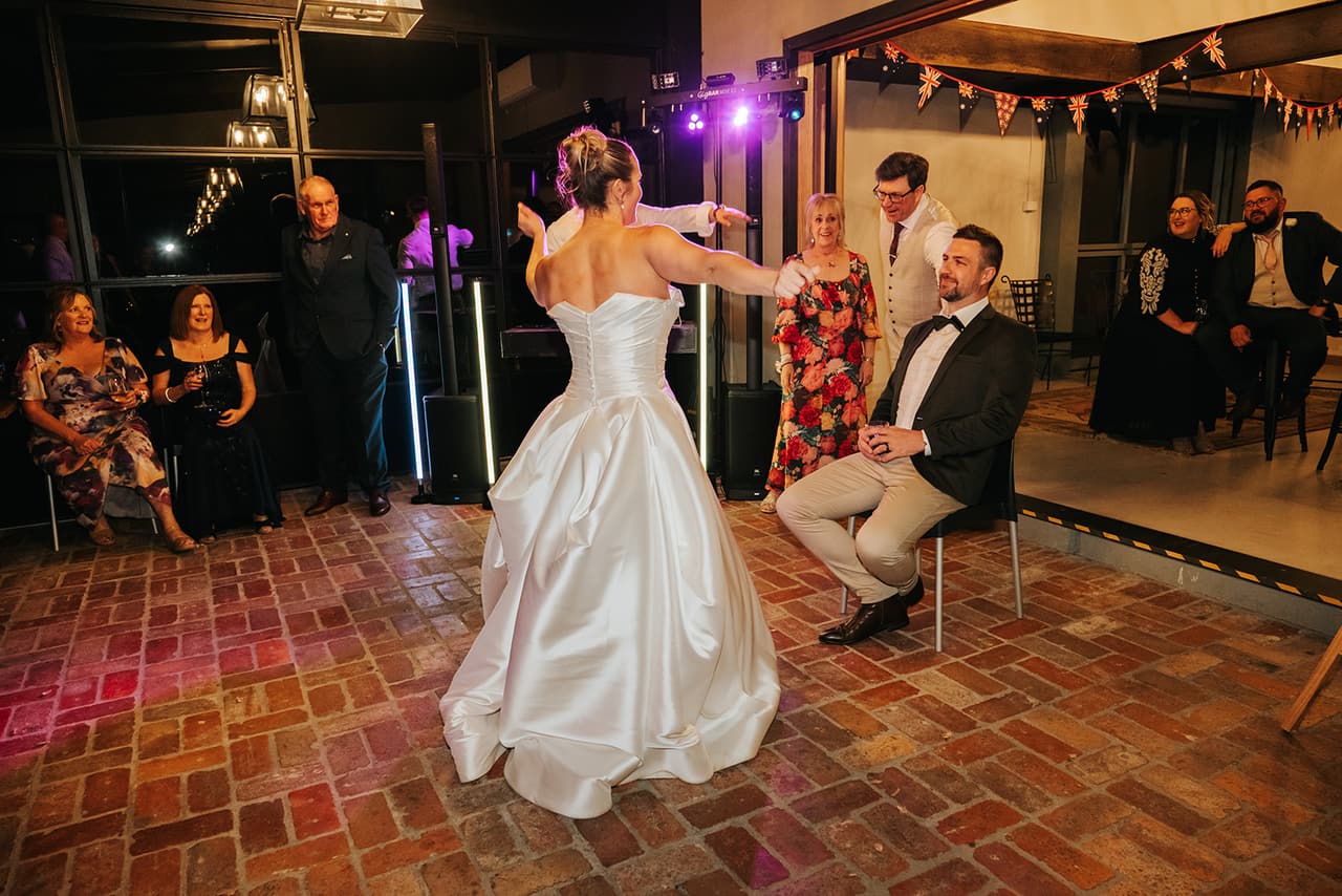 Jessica dancing in front of Max as he sits on a chair in the middle of the dance floor