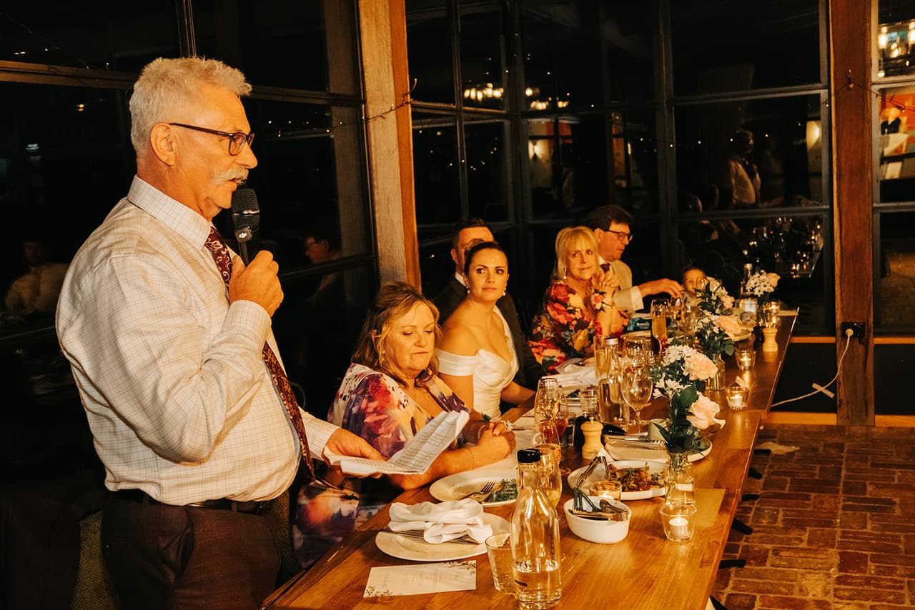 Jessica’s dad giving his speech beside the long table, microphone in hand