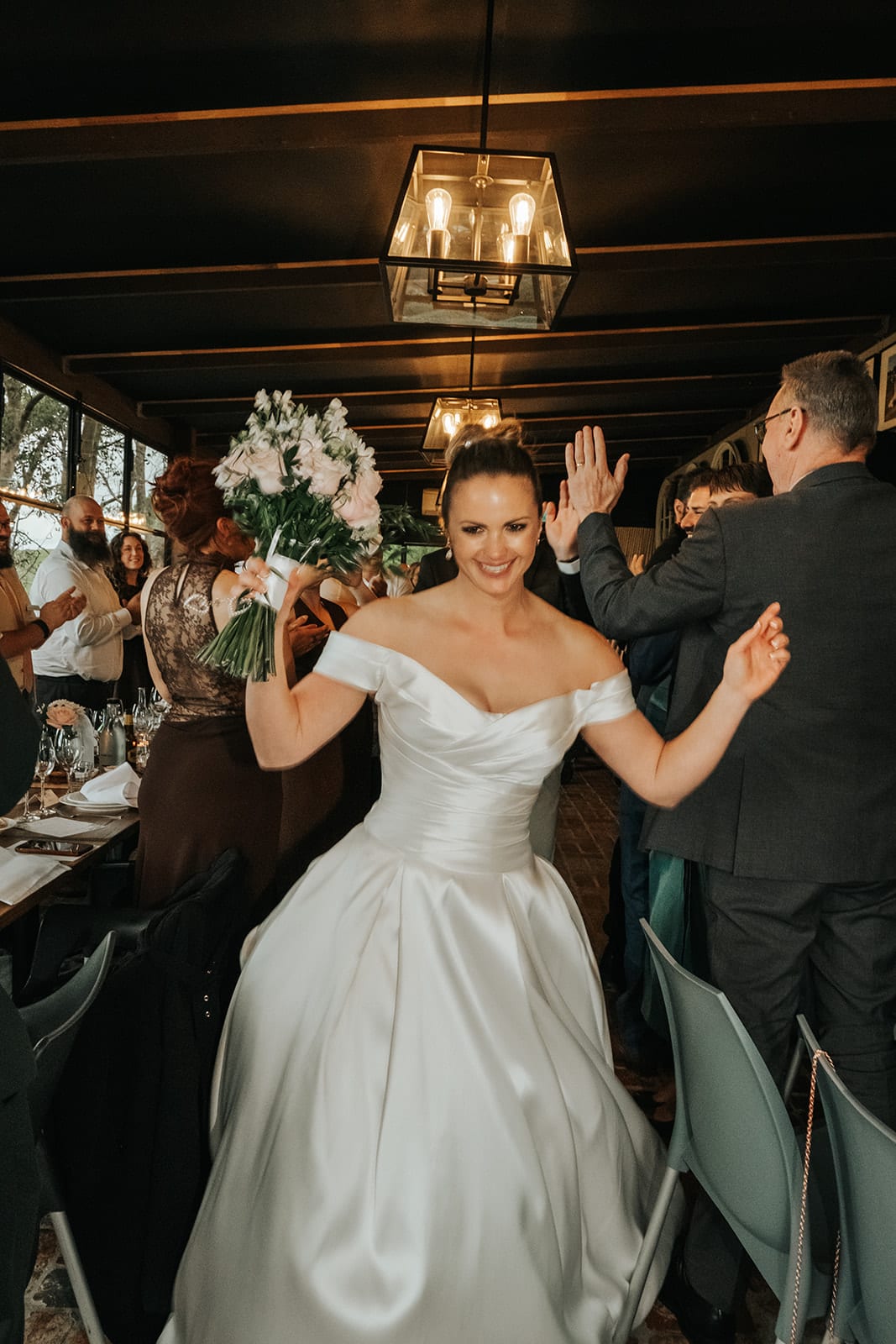 Jessica dancing into the reception with her bouquet raised, Max behind her
