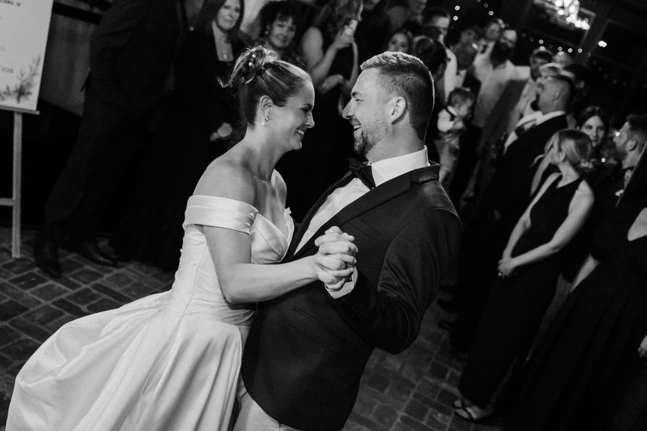 Black and white photo of Jessica and Max dancing close, surrounded by their guests