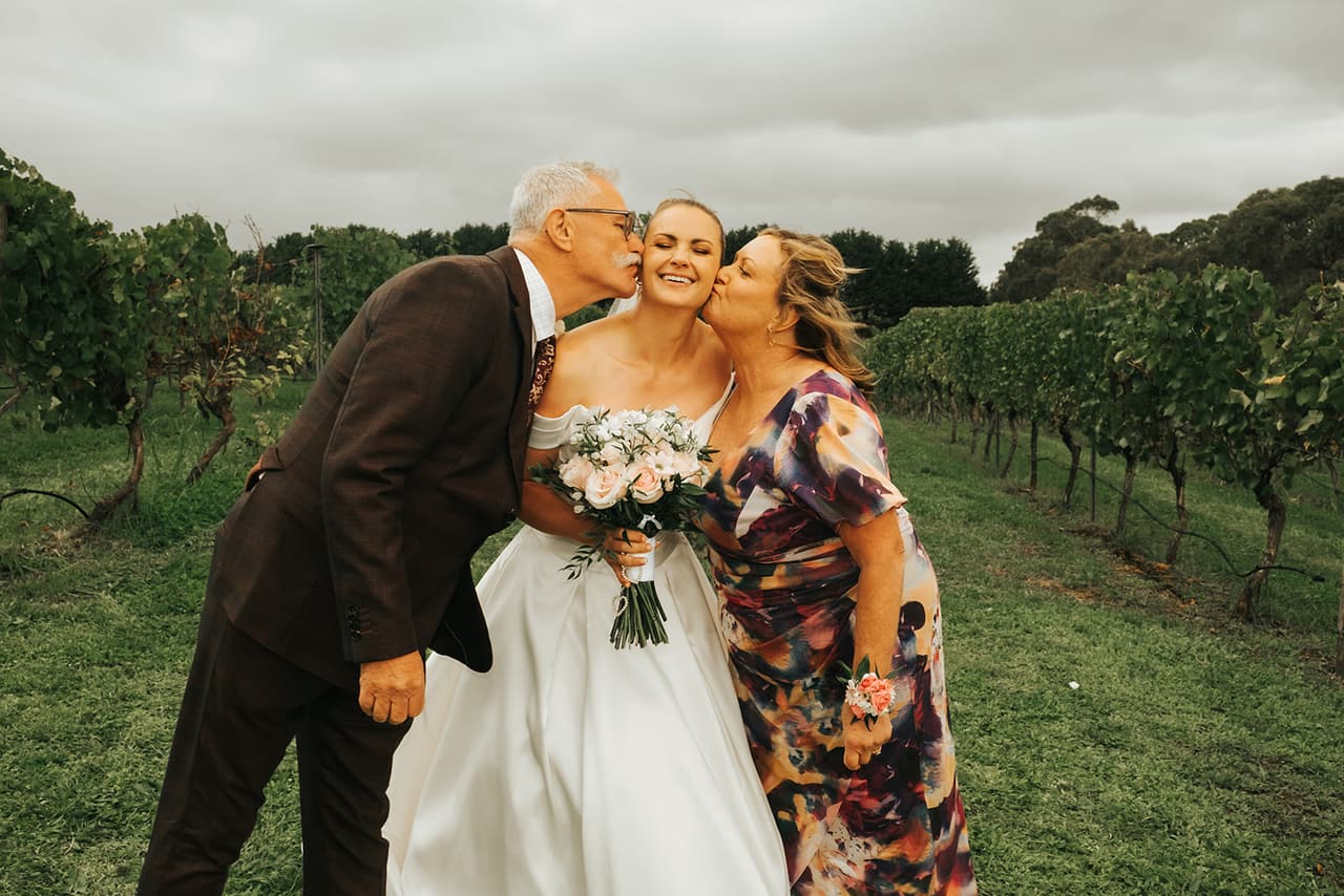 Jessica’s mum and dad kissing her on both cheeks among the vines