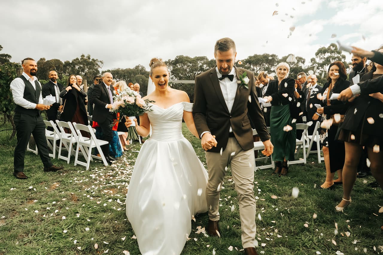 Jessica laughing as she and Max walk back up the aisle through a shower of petals
