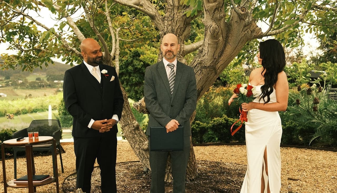 Krish, the celebrant and Joanna standing under a big old tree with the hills behind them