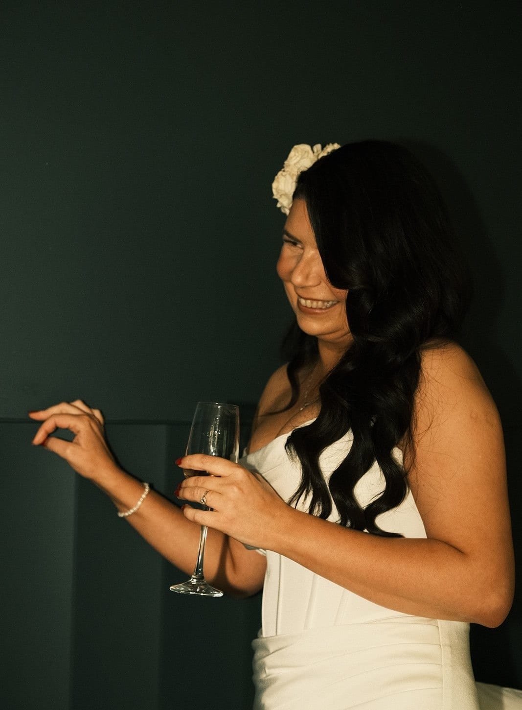 Joanna in her strapless gown with a glass of champagne against a dark green wall