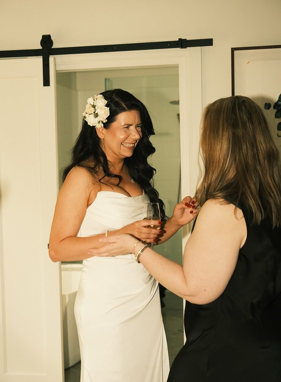 A woman in a black dress fastening the back of Joanna’s gown by a sliding barn door