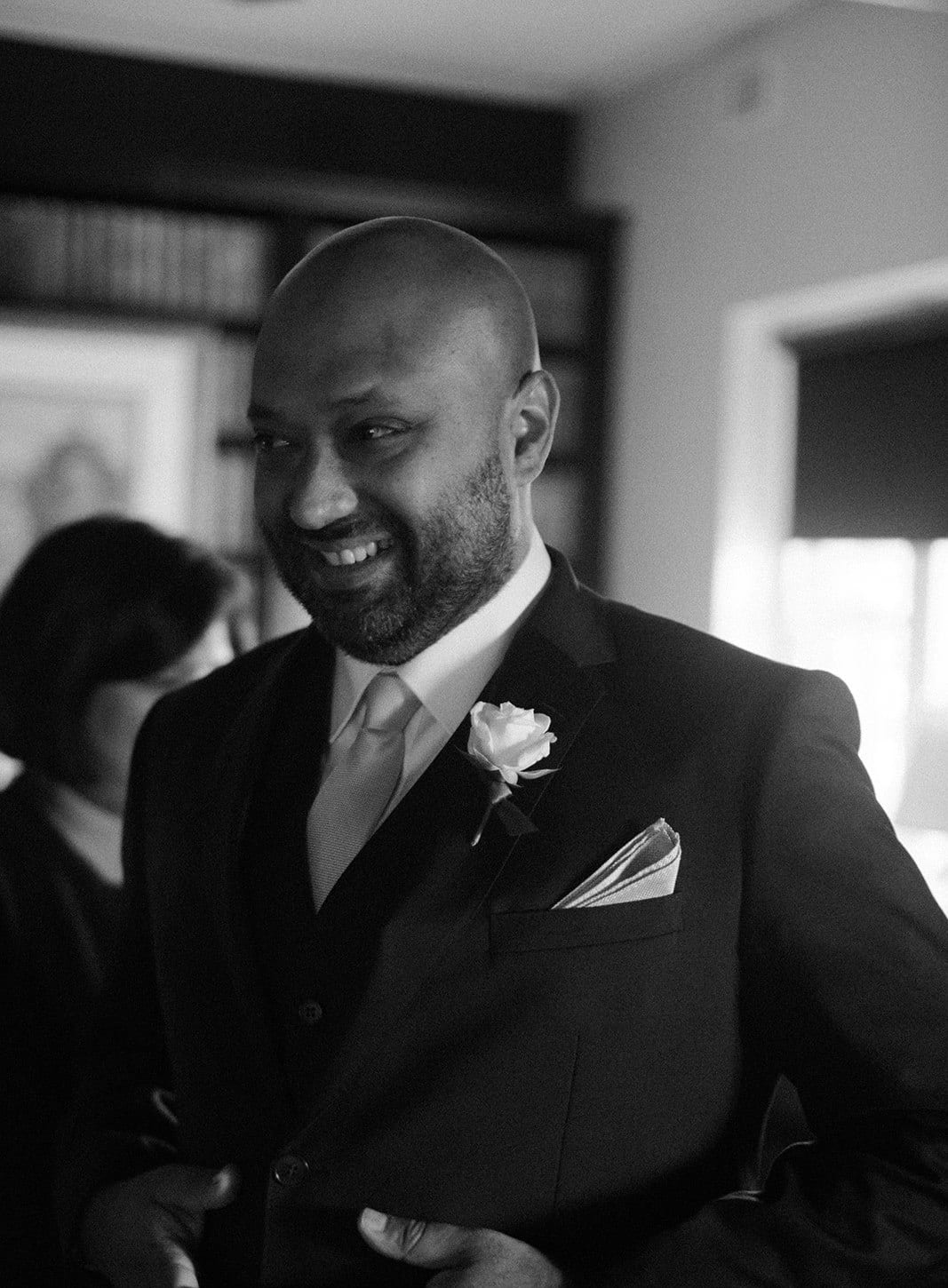 Black and white photo of Krish laughing in his suit and buttonhole