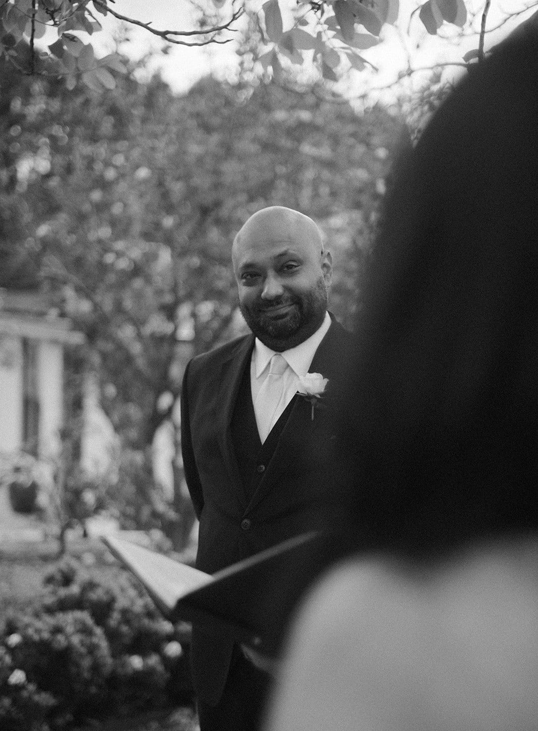 Black and white photo of Krish smiling at Joanna over her shoulder during the ceremony
