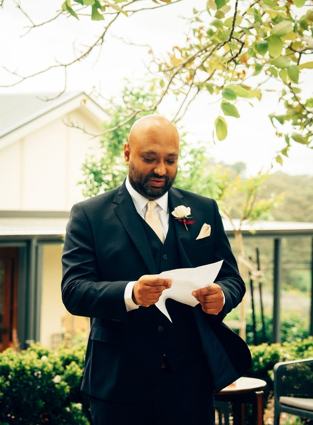 Krish reading his vows from a sheet of paper under the tree