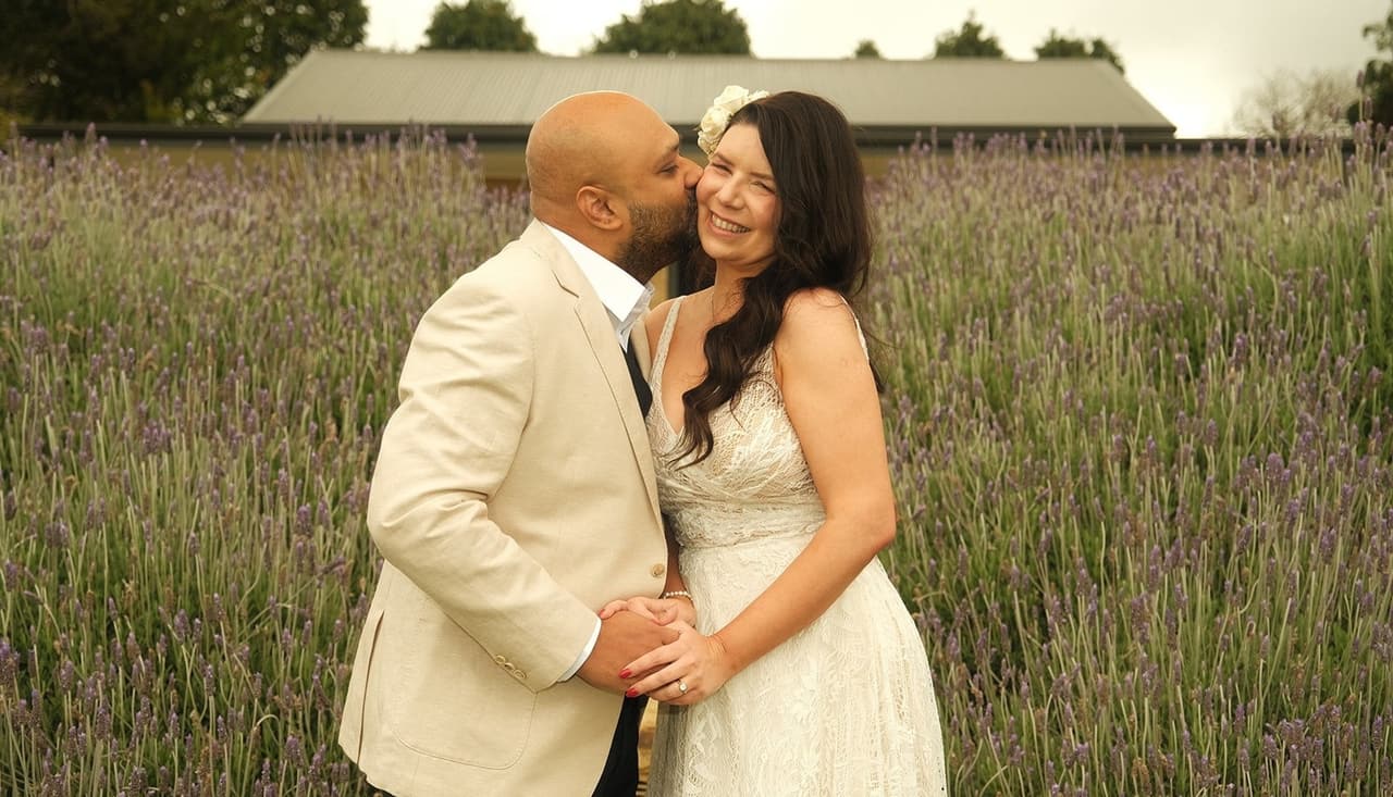 Krish kissing Joanna on the cheek in the lavender as she laughs