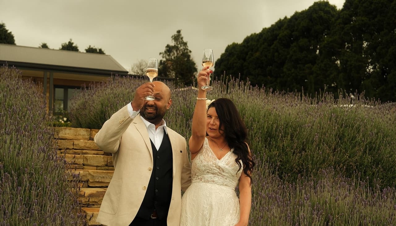 Krish and Joanna raising glasses of champagne beside the lavender and stone steps