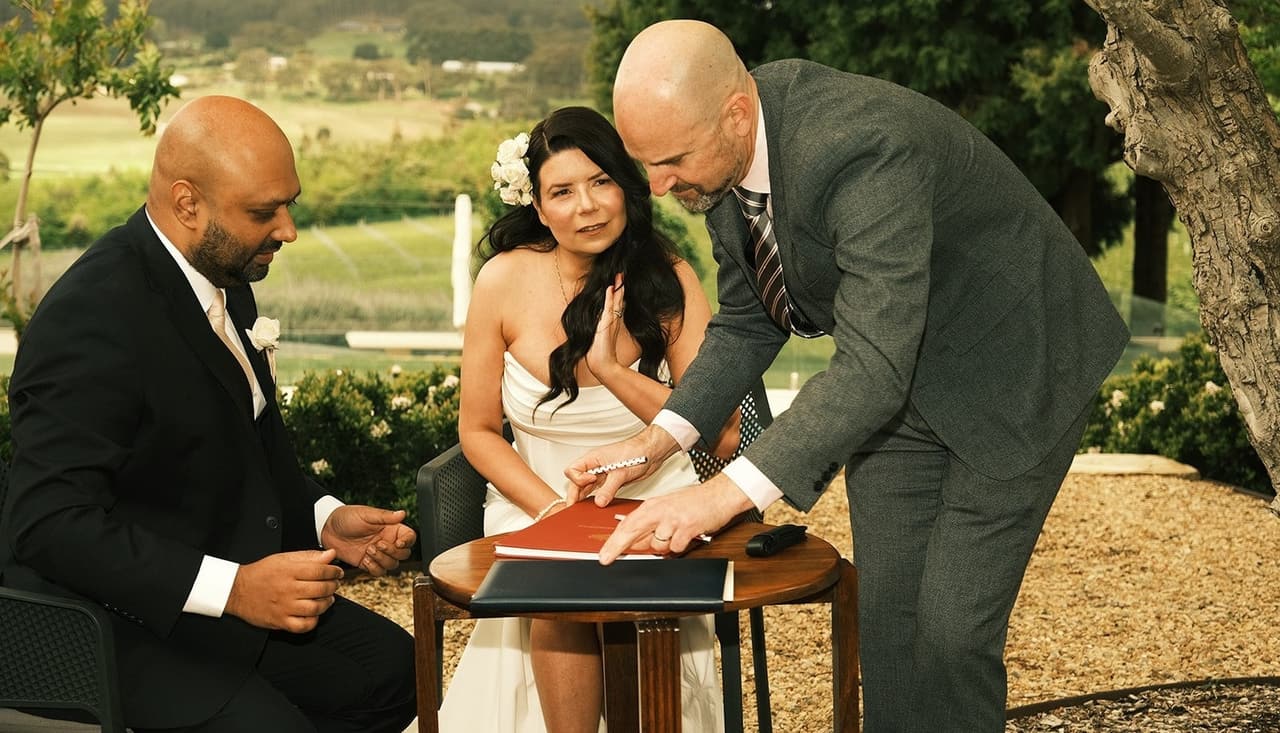 The celebrant showing Krish and Joanna where to sign at a small table in the garden