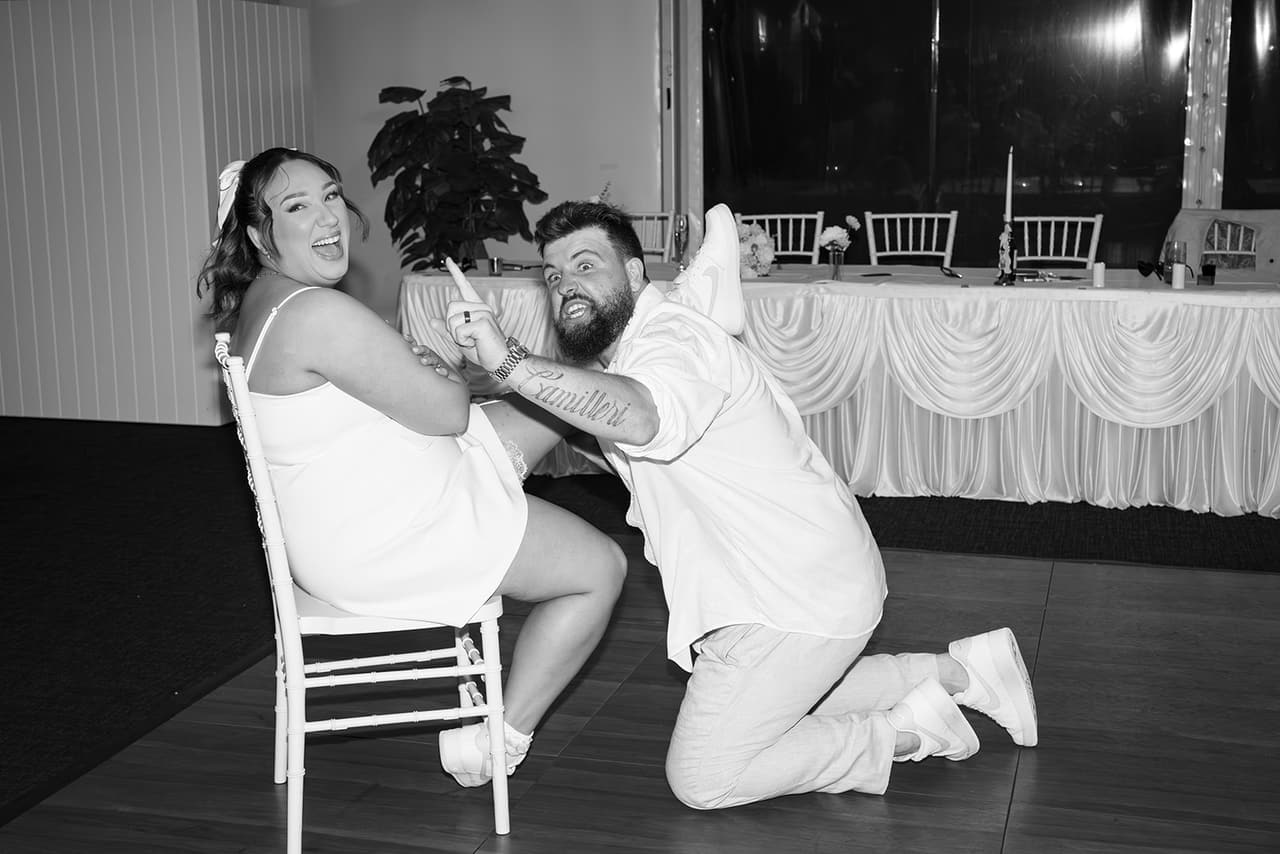 Black and white photo of Karina laughing as Bronson kneels for the garter