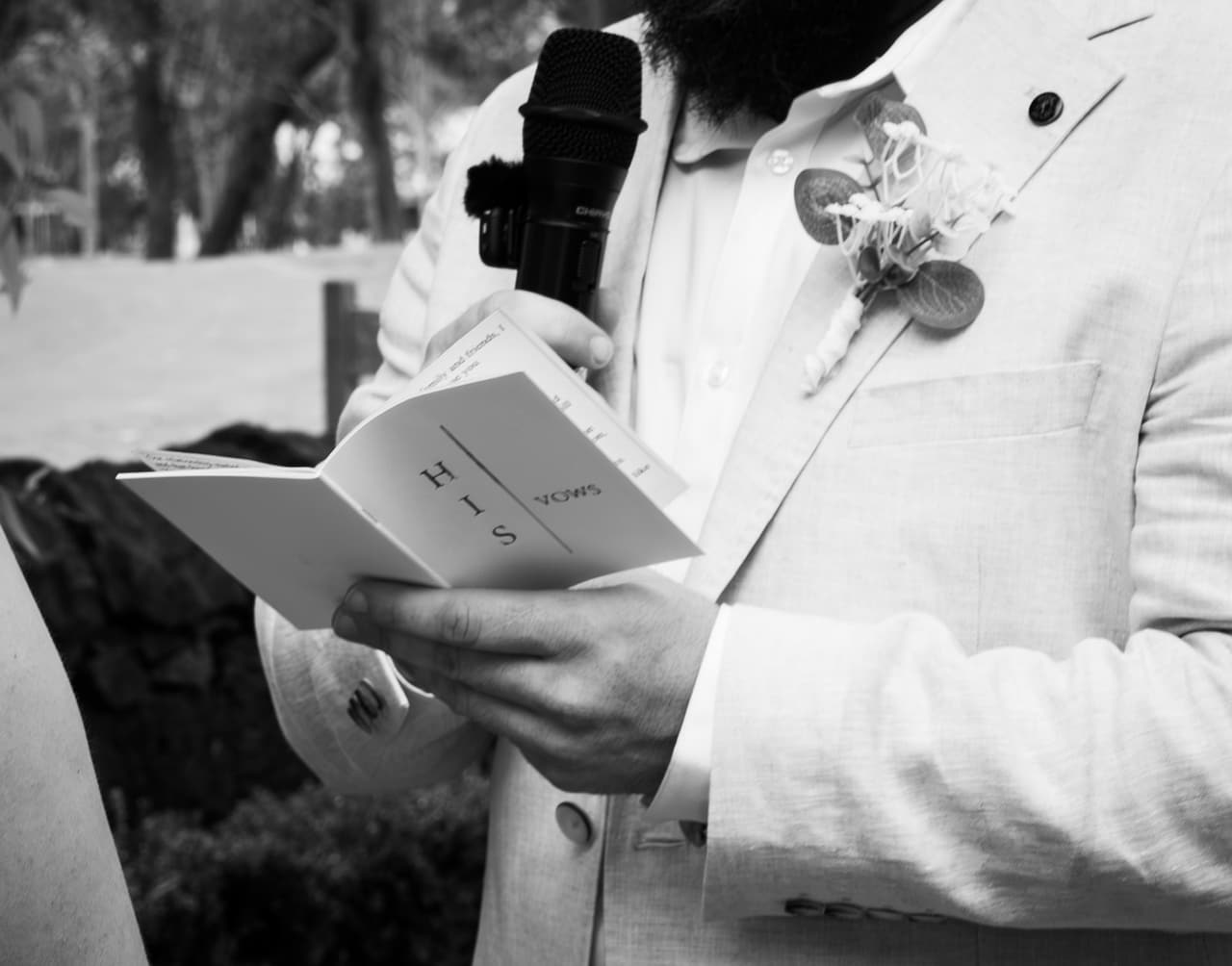 Black and white photo of Bronson holding the microphone and reading from his vows booklet