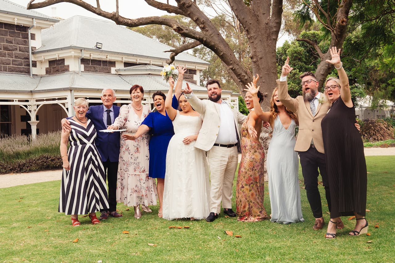 Family cheering with their arms in the air around Karina and Bronson on the lawn in front of the homestead