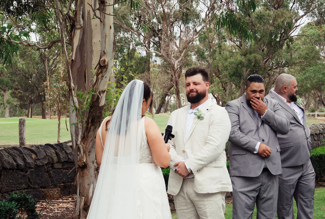 A groomsman covering his mouth as Karina reads her vows to Bronson