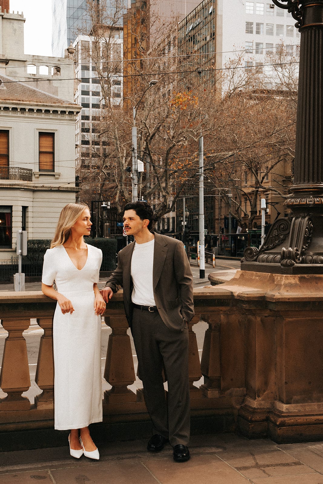Karina and Chris standing at a sandstone balustrade of the Old Treasury Building, the city street behind them