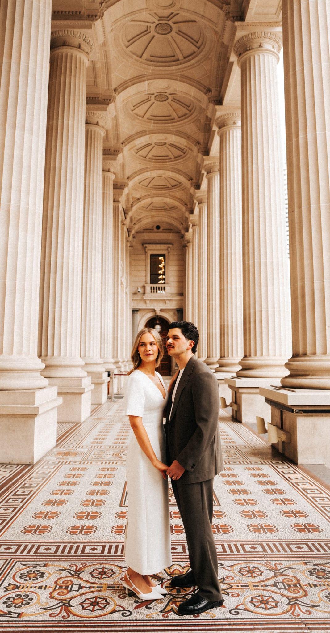 Karina and Chris standing together in the middle of the colonnade, columns and tiles running into the distance