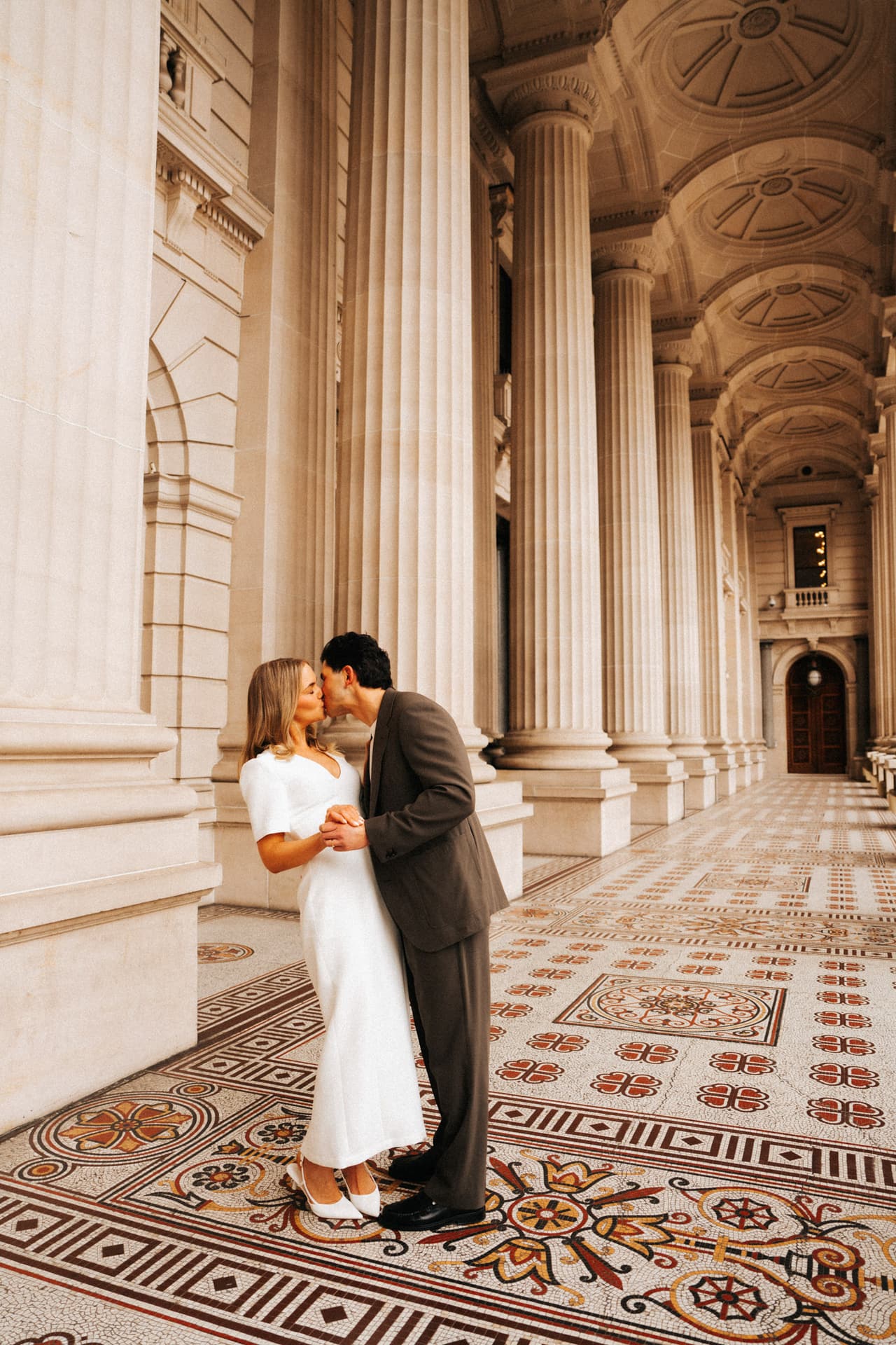 Karina and Chris kissing beneath the vaulted ceiling of the colonnade