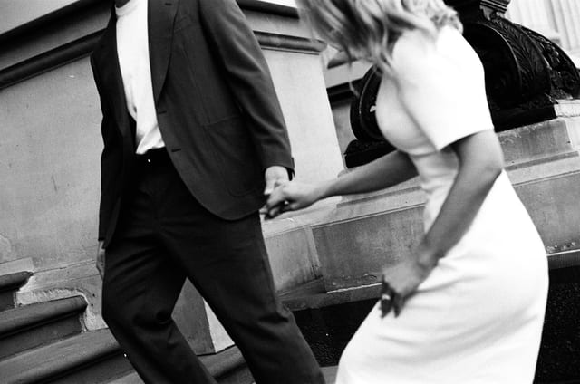 Black and white photo of Karina and Chris climbing the steps hand in hand, on 35mm film