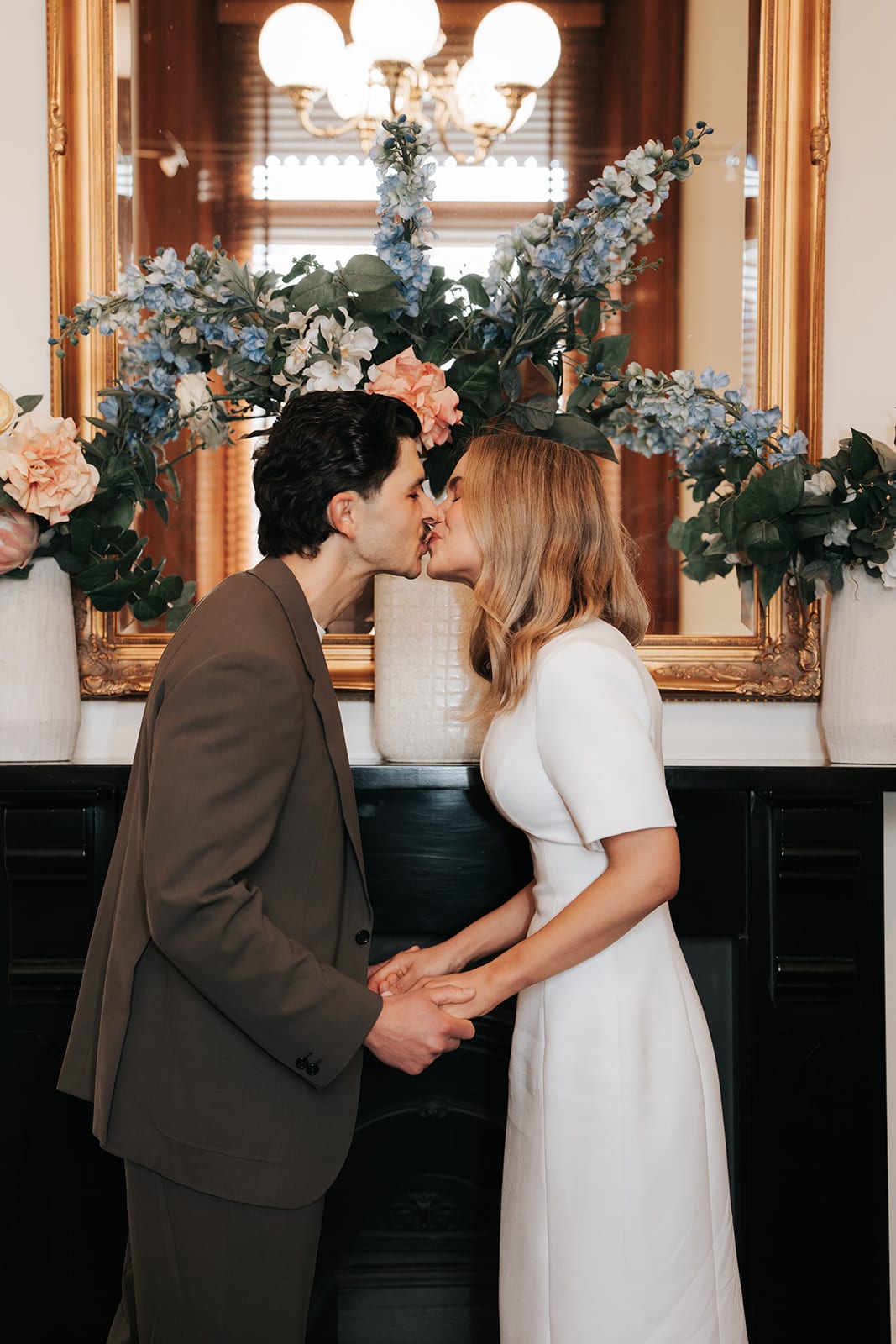Karina and Chris kissing in front of the fireplace, blue and peach flowers on the mantel behind them
