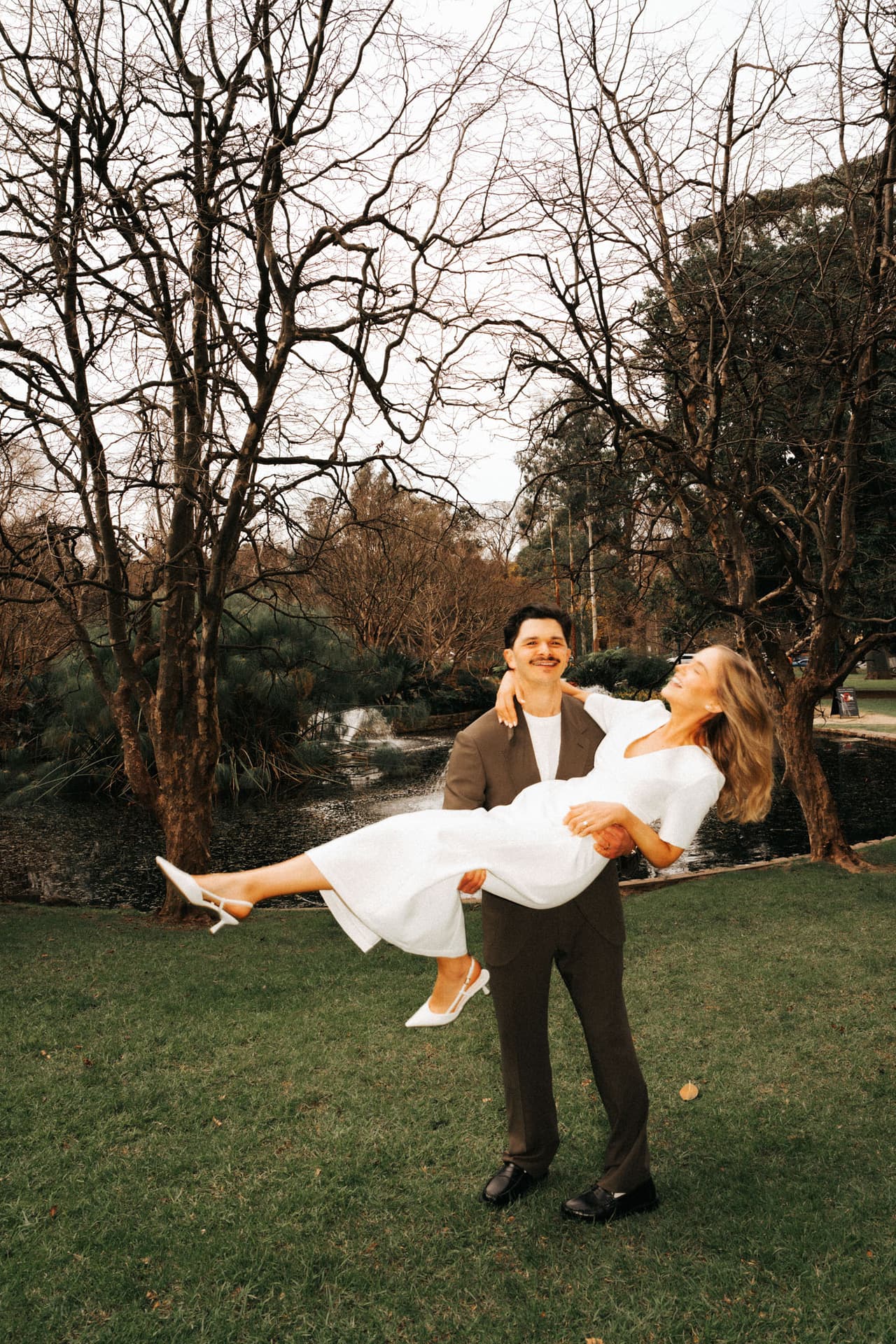 Chris carrying Karina across a lawn among bare winter trees