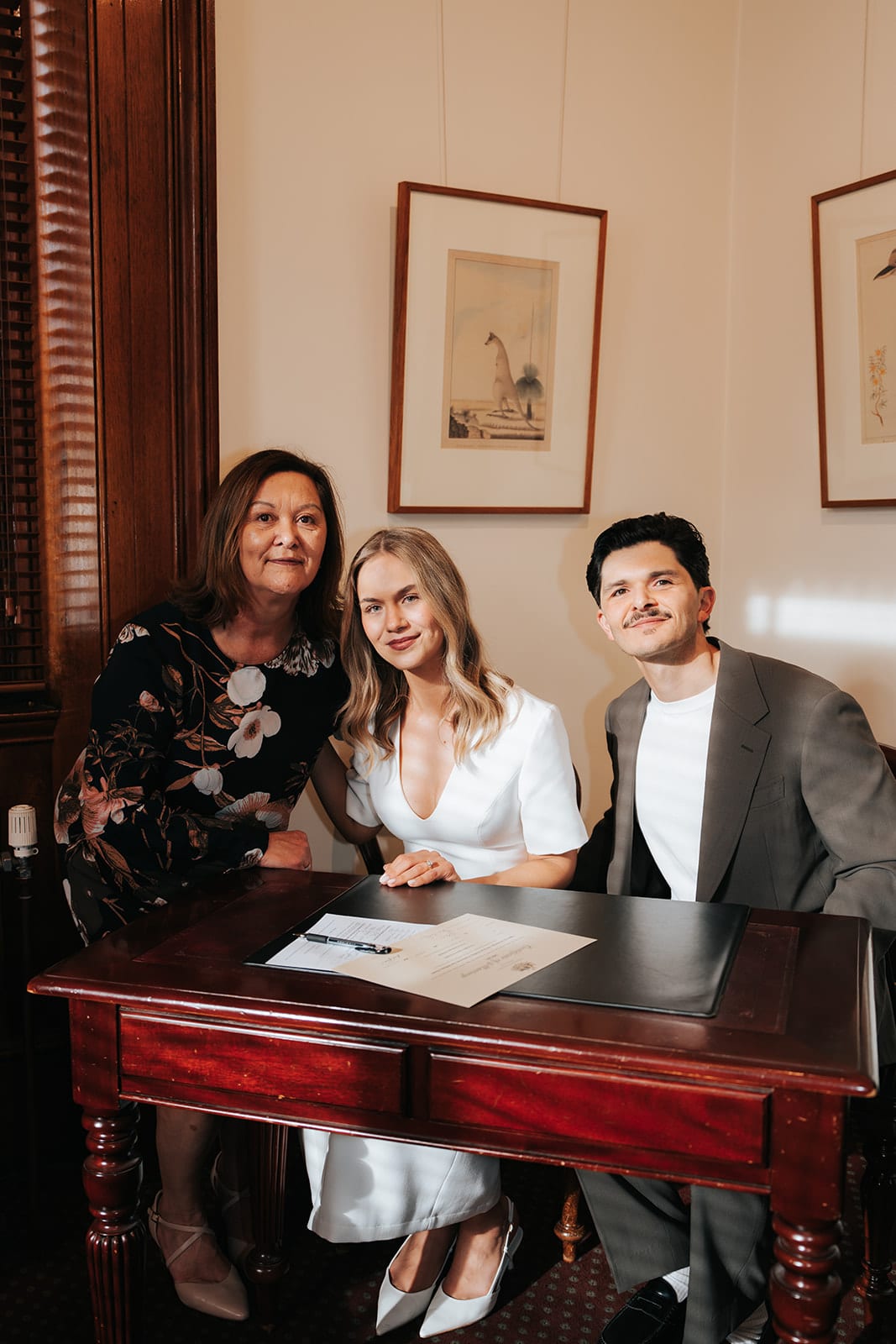 Karina and Chris seated at a red timber desk with one of their mums beside them