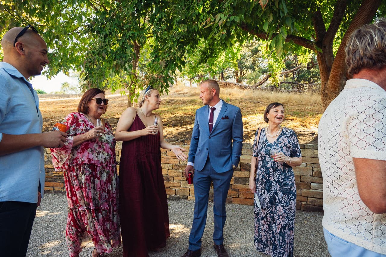 Ben chatting with guests holding drinks on the gravel beside a dry-stone wall