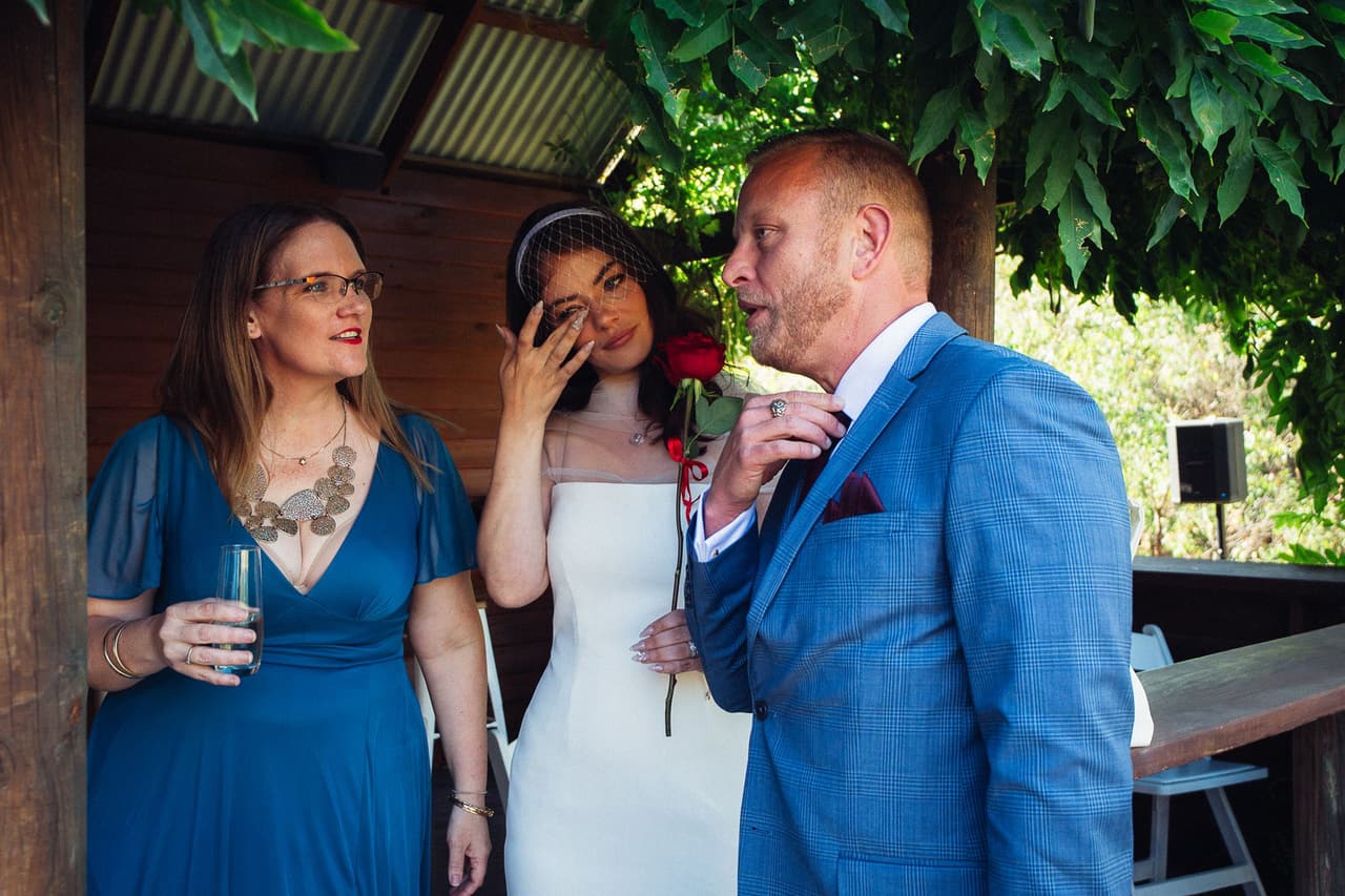 Kim wiping away a tear between Ben and a woman in a blue dress under the Boatshed roof