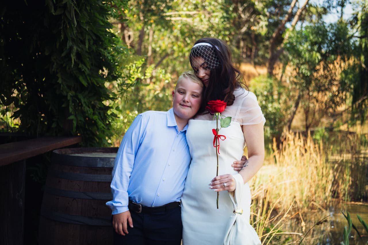 Kim resting her cheek on the head of a smiling boy in a blue shirt on the deck