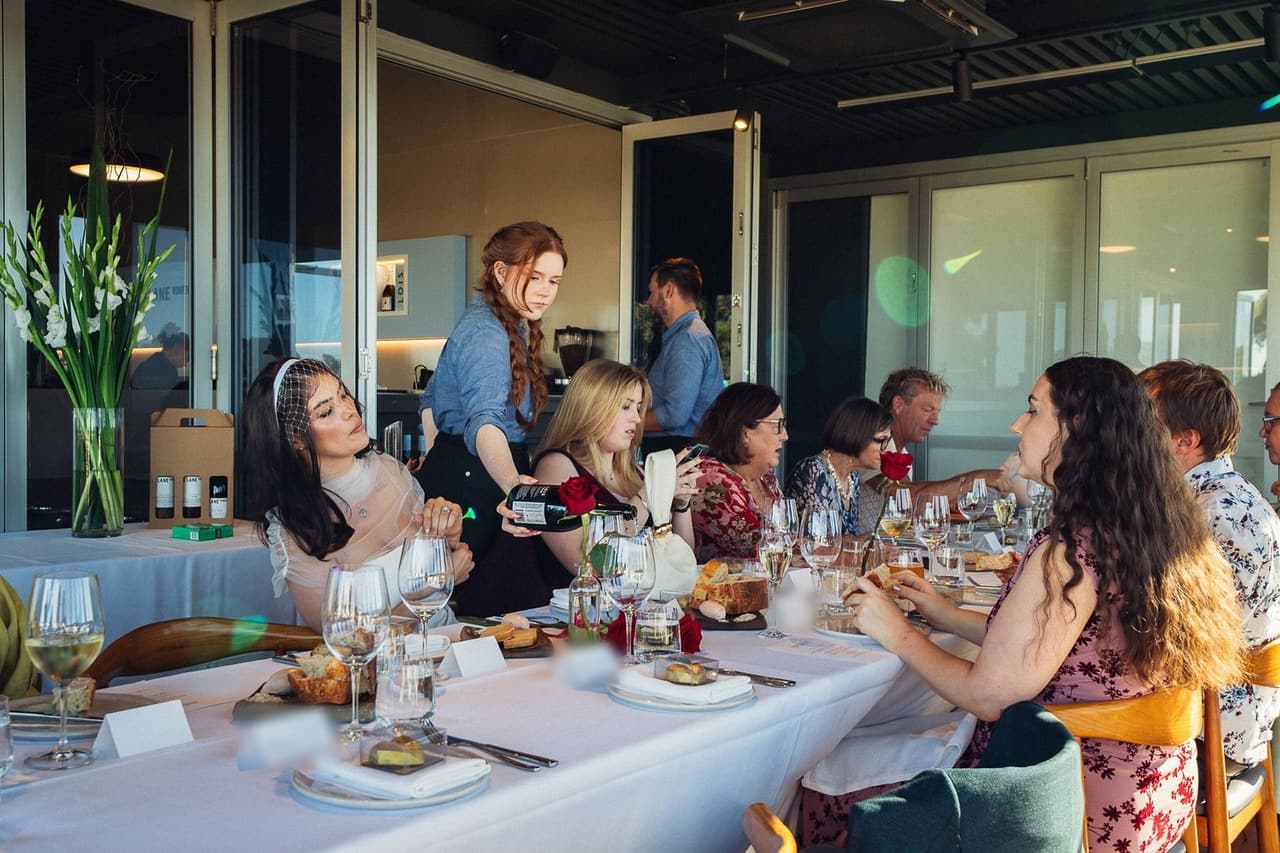 Family and friends at a long table beside wide windows in the evening