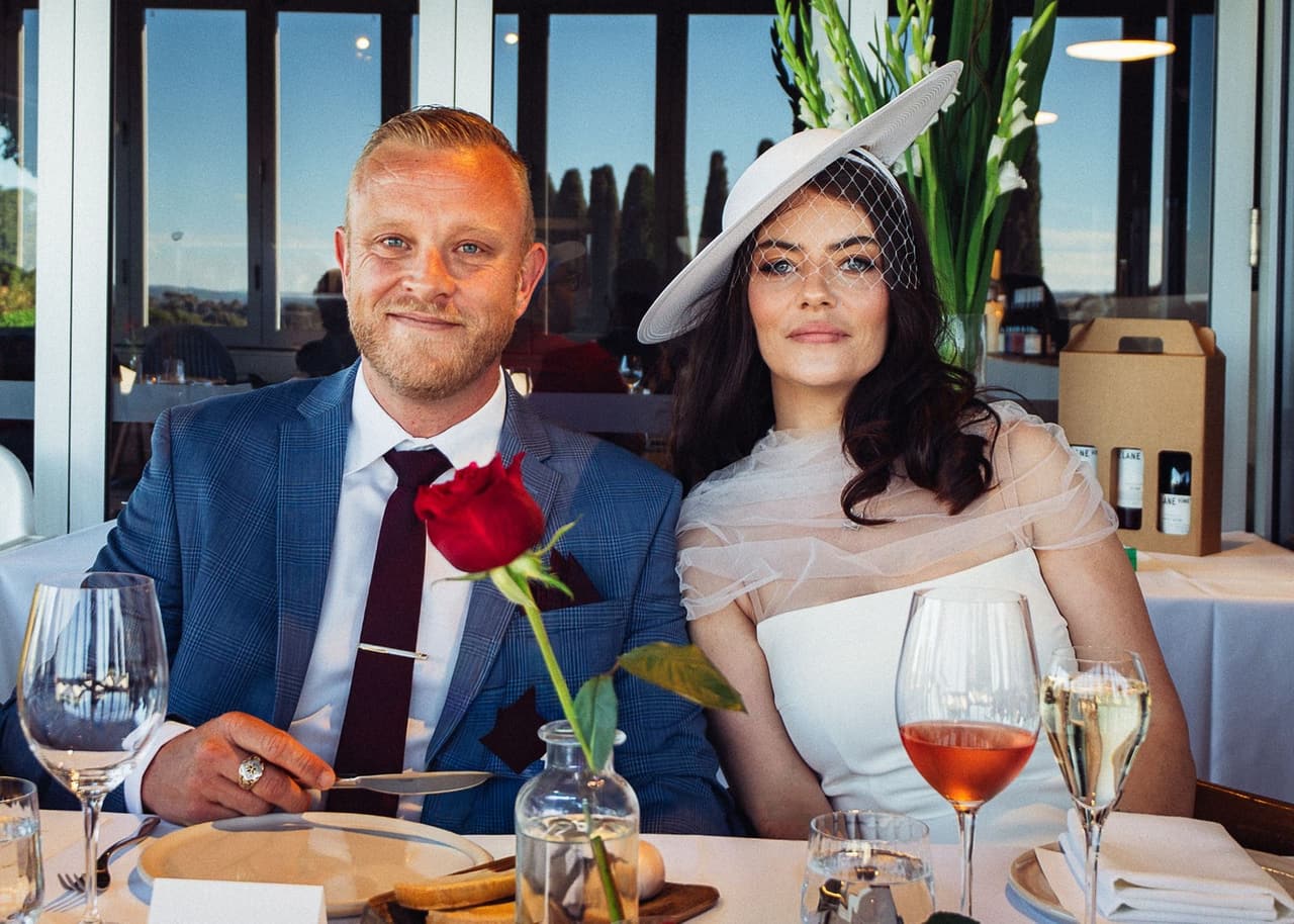 Kim and Ben smiling at the table, a red rose in a vase in front of them