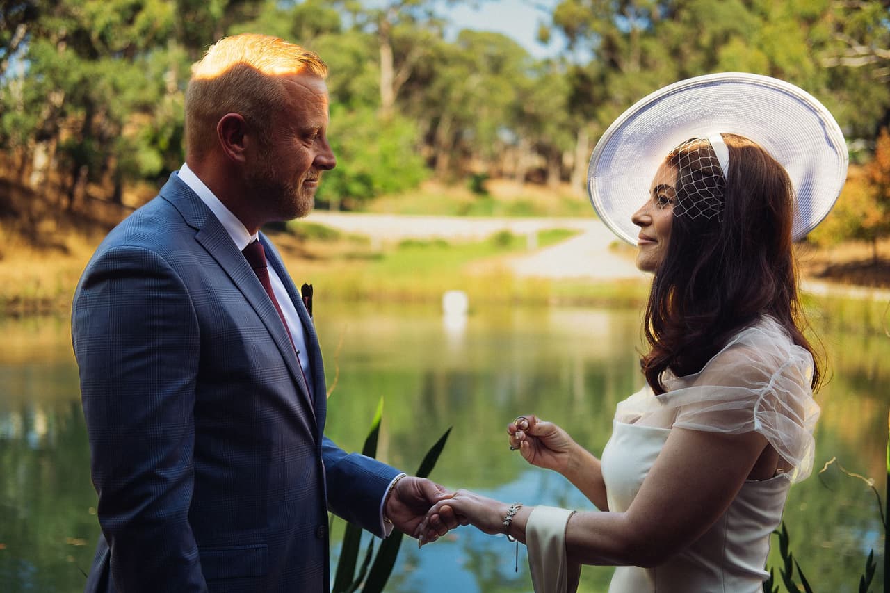 Kim smiling up at Ben with a ring between her fingers as they hold hands by the water
