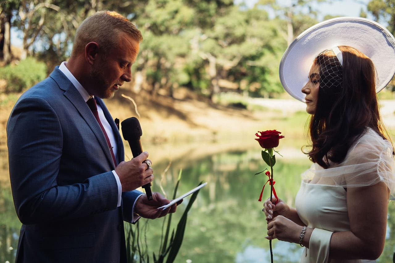 Ben saying his vows into a microphone as Kim listens beside him