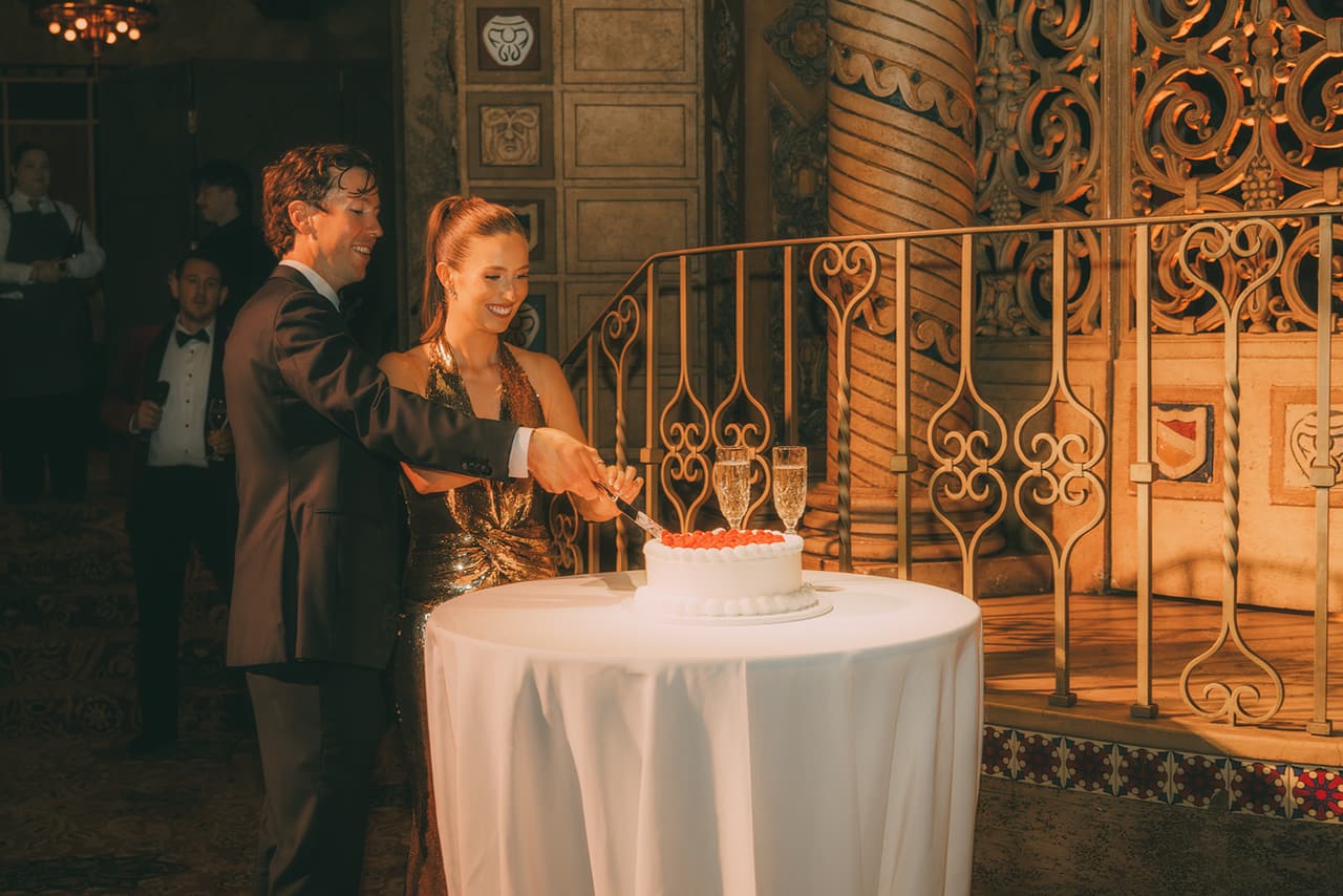 Kira and Nick cutting the cake in front of the ballroom’s ornate iron railing