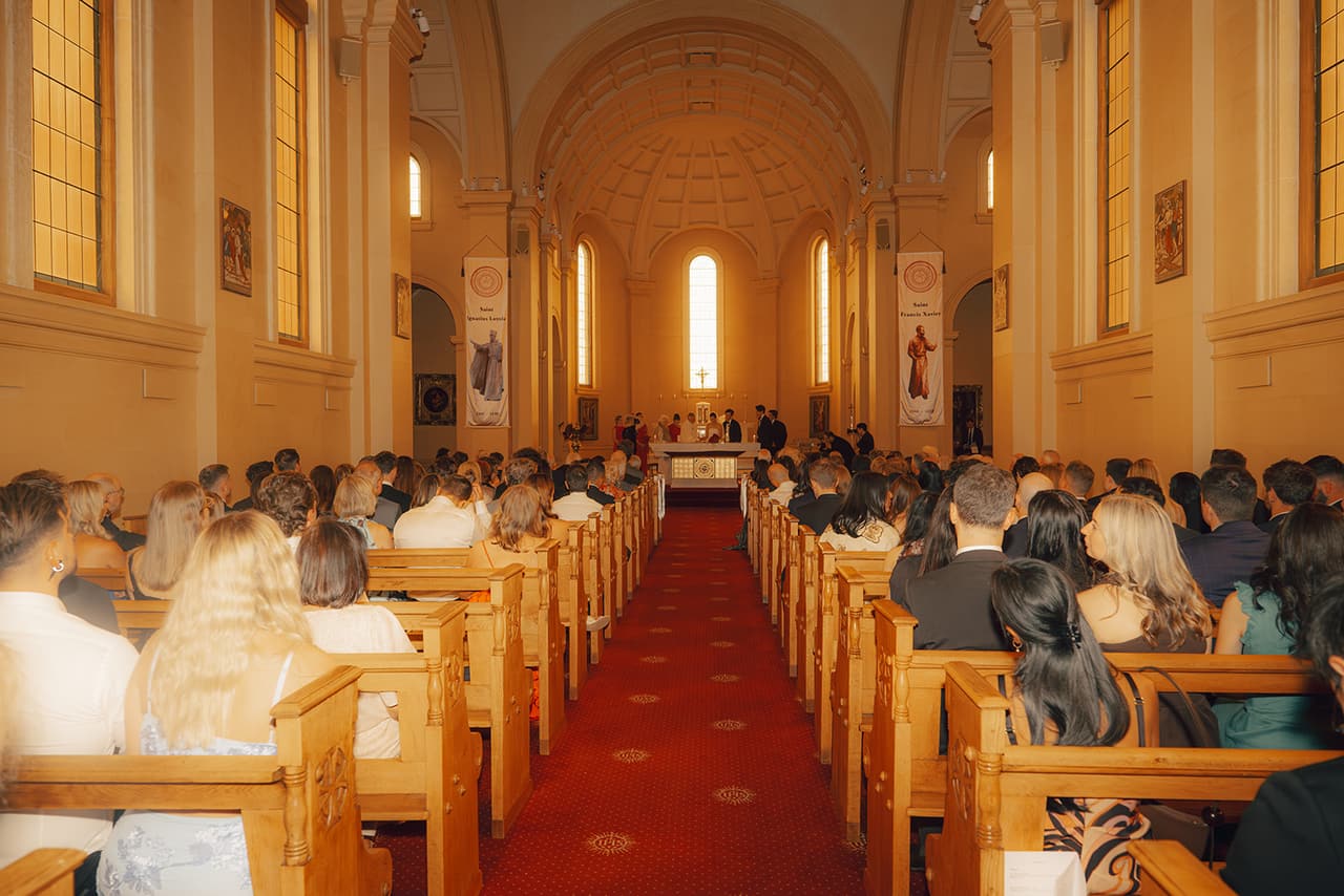 The chapel from the back during the ceremony, guests filling the pews either side of the red aisle
