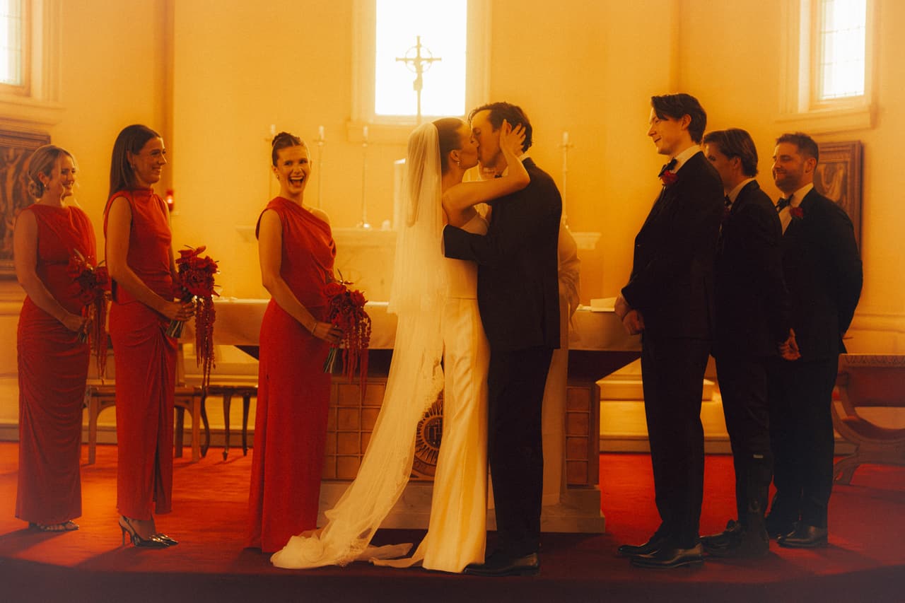 Kira and Nick kissing at the altar, bridesmaids in red on one side and groomsmen on the other