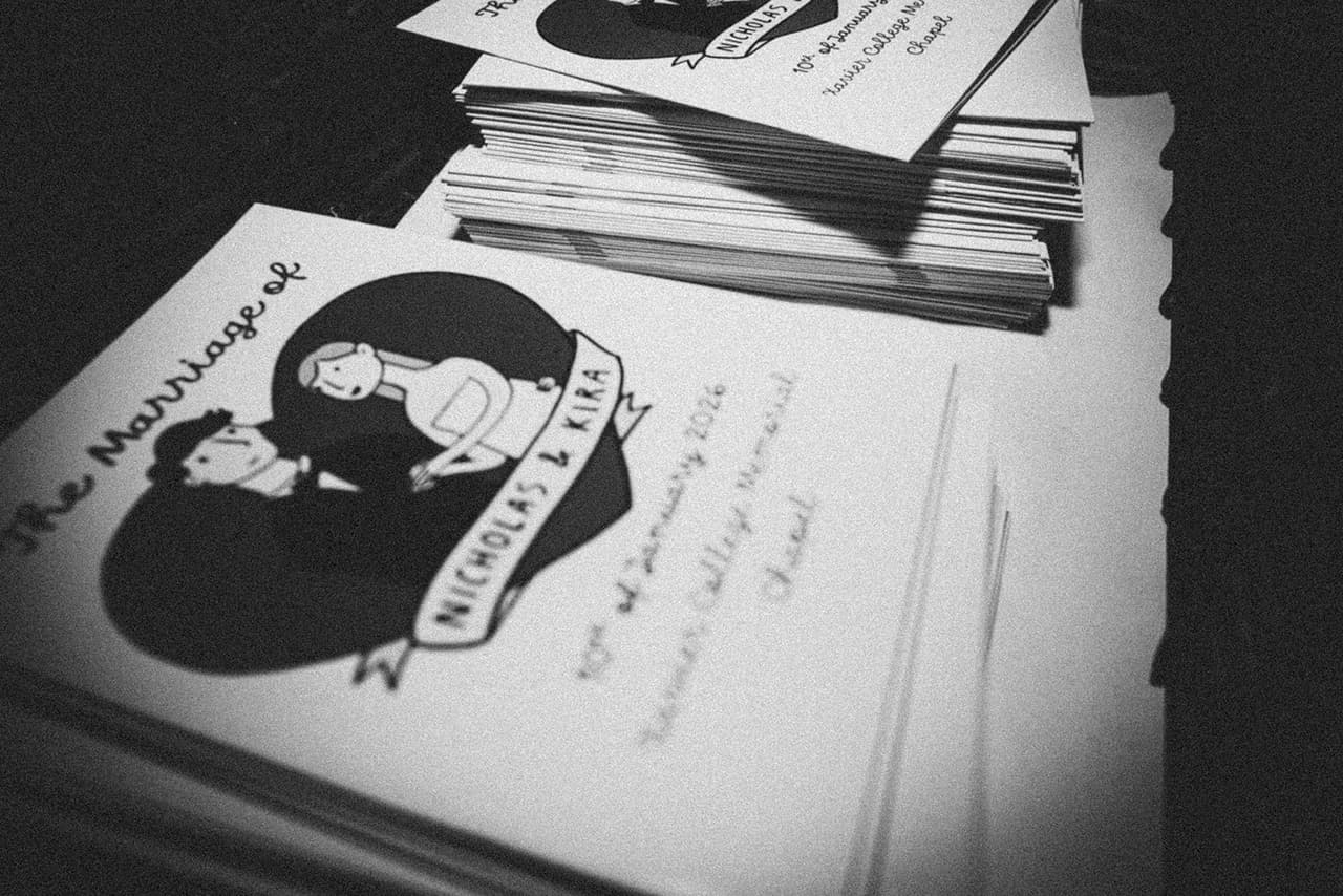 Black and white photo of a stack of orders of service for Nicholas and Kira’s wedding, illustrated with a drawing of the two of them