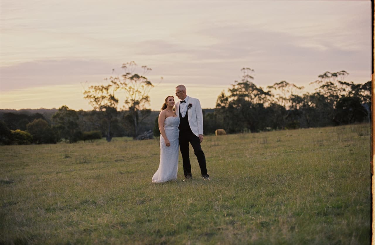 Kristie and Gareth standing together in a wide paddock at Mount Macedon Winery, on 35mm film