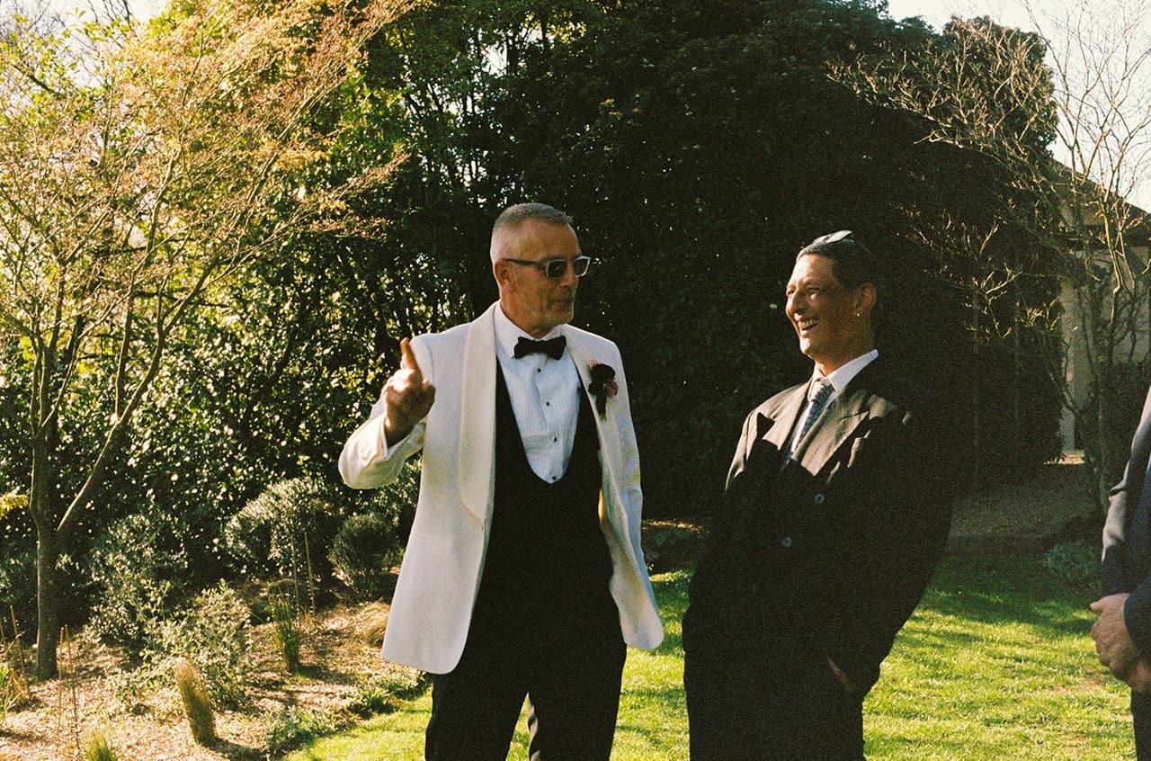 Gareth in his white dinner jacket sharing a laugh with a guest in the garden before the ceremony, on 35mm film