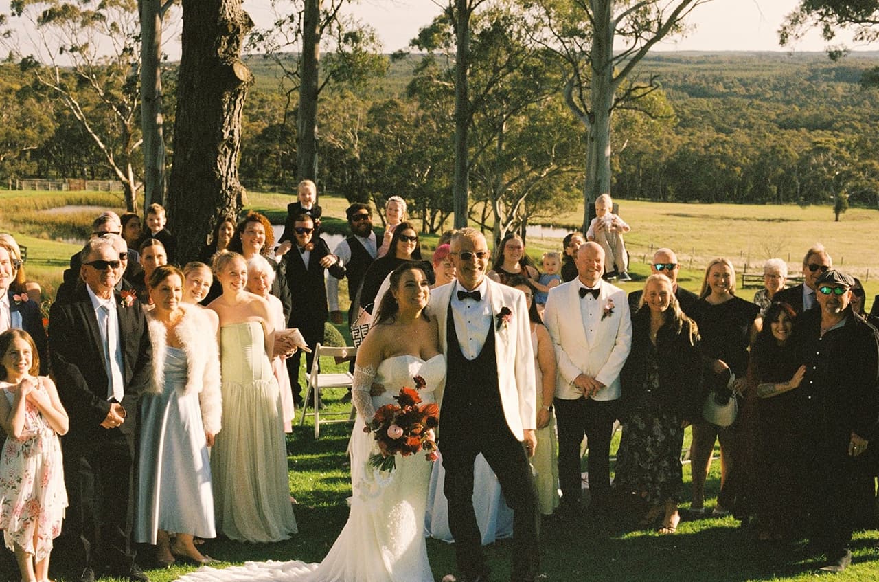 Kristie and Gareth arm in arm at the front of their standing guests after the ceremony, the valley behind them, on 35mm film