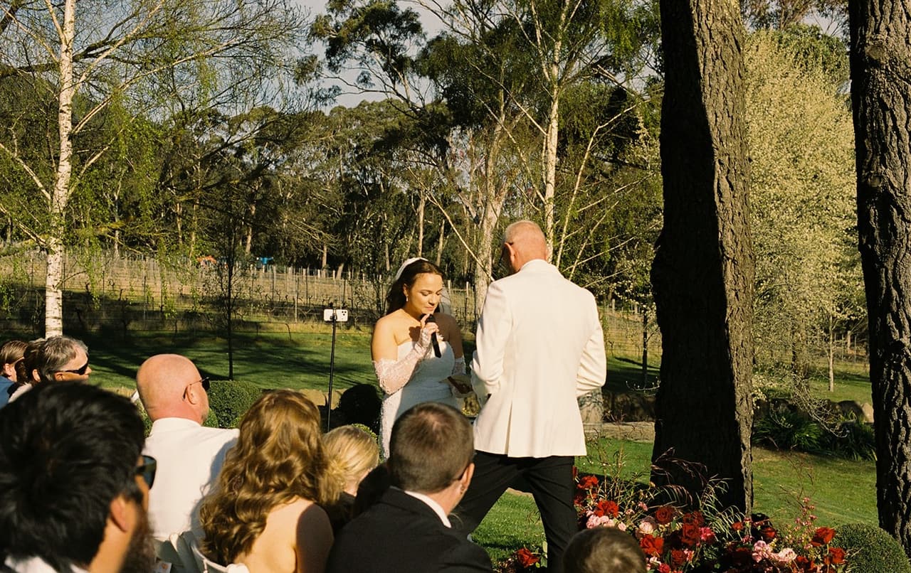 Kristie reading her vows to Gareth beside the flowers, the vines behind them, on 35mm film