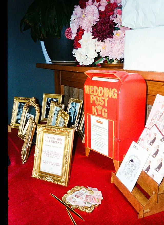 A red wedding post box with their initials among gold-framed family photos, on 35mm film