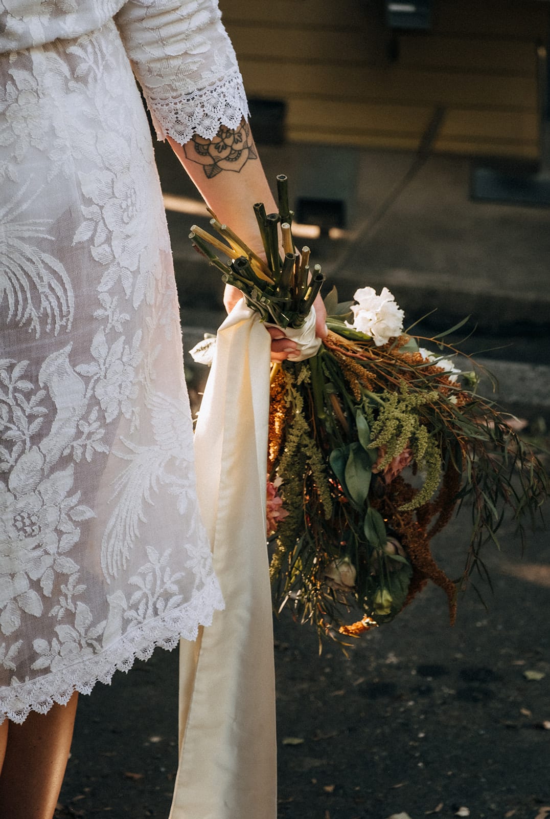 Lana’s bouquet of dried flowers and long cream ribbons against her lace dress