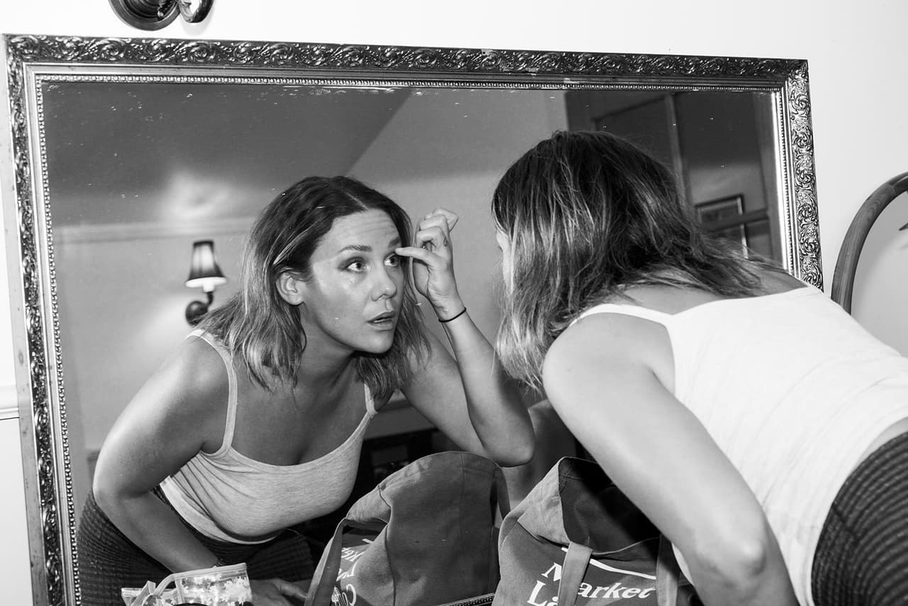 Black and white photo of two women doing their makeup in a big gilt mirror