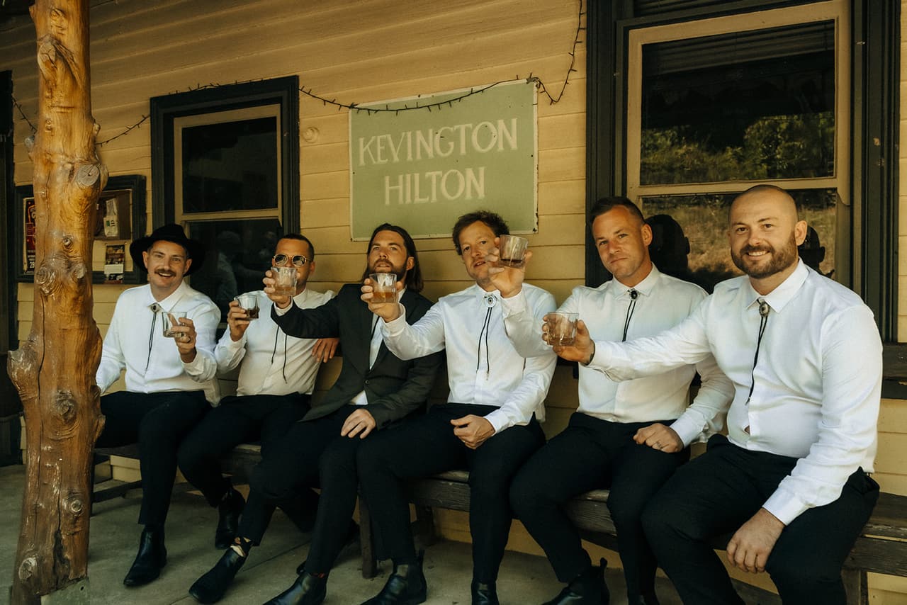 The groomsmen lined up on a bench under a hand-painted Kevington Hilton sign
